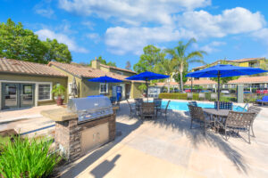 outdoor grill with seating areas, blue umbrellas, and pool in the background