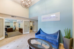 lobby entrance way with blue couch against light blue wall, coffee table, Avanath logo sign, and modern chandelier