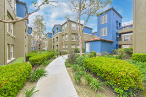 Exterior Overlook at Anaheim Hills, beige and blue residential buildings, meticulous landscaping, bench along sidewalk, lush foliage, photo taken on a sunny day.