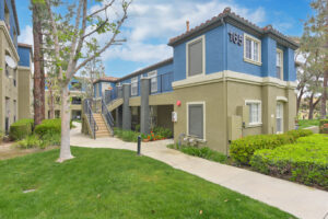 Exterior Overlook at Anaheim Hills, beige and blue residential buildings, meticulous landscaping, bench along sidewalk, lush foliage, photo taken on a sunny day.