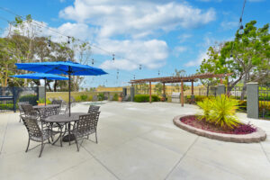 Exterior patio area, hot tub, grilling area, patio tables with umbrellas, photo taken on a sunny day.