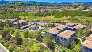 Aerial Exterior of Overlook at Anaheim Hills community center and residential buildings, lush foliage, meticulous landscaping, sprawling hills in the background, photo taken on a sunny day.