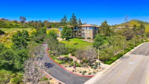 aerial exterior of the the Overlook at Anaheim hills entrance, street view signage, road leading up the hill to the apartment community, meticulous landscaping, lush foliage, sprawling hills in the background, photo taken on a sunny day.