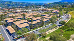 aerial exterior of the Overlook at Anaheim hills, beige and blue residential buildings, meticulous landscaping, lush foliage, sprawling hills in the distance, photo taken on a sunny day.