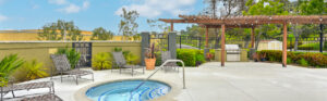 Exterior Hot Tub, lounge chairs around hot tub, grilling area in background, pergola, photo taken on a sunny day.