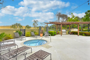 Exterior Hot Tub, lounge chairs around hot tub, grilling area in background, pergola, photo taken on a sunny day.